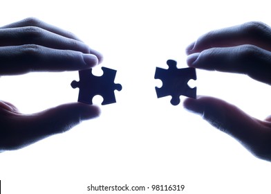 business partners combining puzzle pieces against bright light