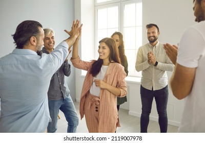 Business Partners Making A Deal. Two Happy Smiling Cheerful People Give Each Other A High Five While Coworkers Are Applauding. Team Of People Meeting In Modern Office. Teamwork And Partnership Concept