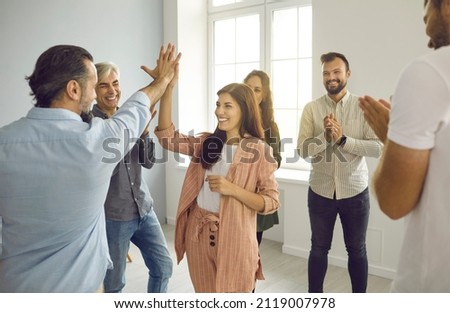 Business partners making a deal. Two happy smiling cheerful people give each other a high five while coworkers are applauding. Team of people meeting in modern office. Teamwork and partnership concept