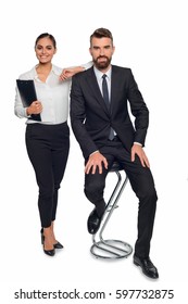 Business Partners Pose For A Photo. Young Woman Leans On A Shoulder Of Her Colleague Sitting On A Barstool. They Both Wear Clothes In Strict Style. Vertical Full Body Shot.