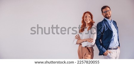 Business partners posing in front of gray background, looking at camera and smiling.