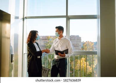 Business Partners In Protective Sterile Mask Shake Hands After Contract Meeting Near Modern Elevator. Business Etiquette, Congratulation, Merger And Acquisition Concepts. Covid-19.