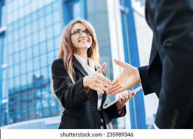 Business partners shake hands, standing in front of his office.