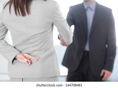 Business Partners Shaking Hands With One Of Them Holding Her Fingers Crossed Behind Her Back.