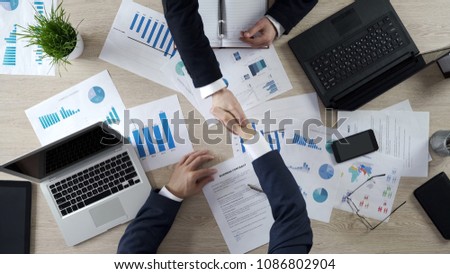 Business partners shaking hands, signing business contract after negotiations
