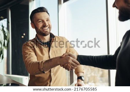 Business partnership. Smiling male entrepreneurs shaking hands, celebrating cooperation agreement at office. Two happy businessmen handshaking after successful deal at modern company
