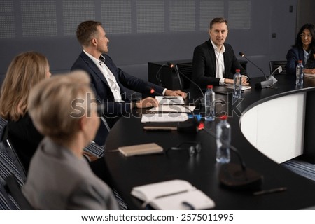 Business people at boardroom meet in modern international center. Microphone speech of Caucasian man as economy expert at conference forum. Presentation group works at debate indoor in convention hall