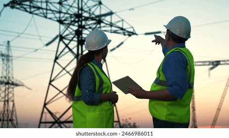 Business people, builders energy construction. Two energy engineers work on tablet computer outdoors. Engineers in helmets, on field with electrical towers, working together. Electricity voltage pylon - Powered by Shutterstock