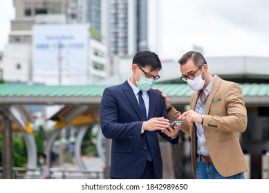 Business People Caucasian With Asian Man Office Worker Colleague Partnership Wearing Protective Face Mask For Protect Covid-19 Virus Discussing Business Project Plan With Using Smartphone In The City.