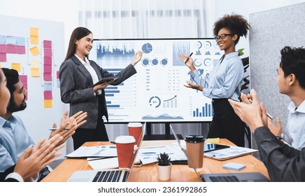 Business people celebrate after successful presentation or meeting on data analysis display on TV screen. Happy team gathers in office room, cheer to collaboration with celebratory gesture. Concord