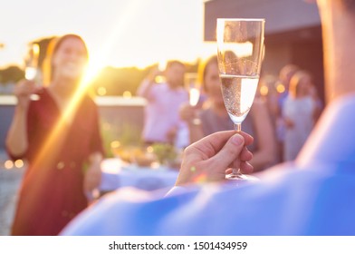 Business People Celebrating Success While Raising Champagne Glasses Together At Rooftop Party With Yellow Lens Flare In Background