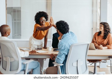 Business people celebrating a successful project with a high five in a boardroom. Business men and women showing teamwork, collaboration, and creativity in a diverse workplace environment. - Powered by Shutterstock