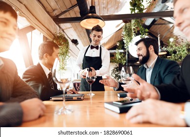 Business people chatting while a waiter pours wine into glasses. Men in a suit sitting in a restaurant and chatting on business. - Powered by Shutterstock