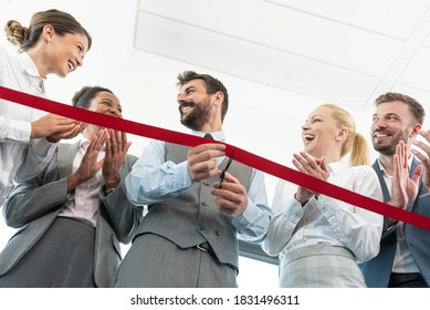 Business People Clapping Hands While Businessman Is Cutting Red Ribbon At New Office