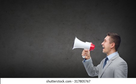 business, people, communication and public announcement concept - happy businessman in suit speaking to megaphone over dark gray concrete wall background
