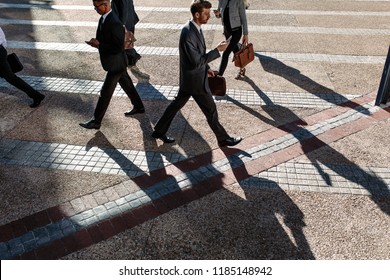 Business People Commuting To Office In The Morning Carrying Office Bags And Using Mobile Phones. Businessmen In A Hurry To Reach Office Walking On City Street Using Their Mobile Phone.