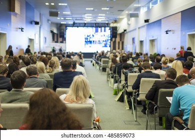 Business People Concept And Ideas. Large Group Of People At The Conference Watching Presentation On A Big Screen In Front. Horizontal Image Orientation