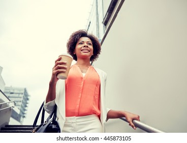 business and people concept - young smiling african american businesswoman with coffee cup going down stairs into city underpass