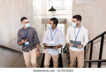 business, people and corporate concept - businessmen in protective medical masks with name tags walking up office stairs and talking