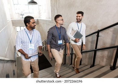 business, people and corporate concept - men with conference badges, folder, tablet pc computer and smartphone walking up office stairs - Powered by Shutterstock
