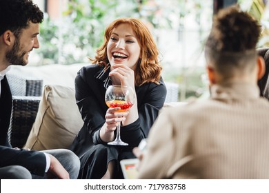 Business people are enjoying drinks together in a bar courtyard after work. They are laughing and talking while drinking cocktails.