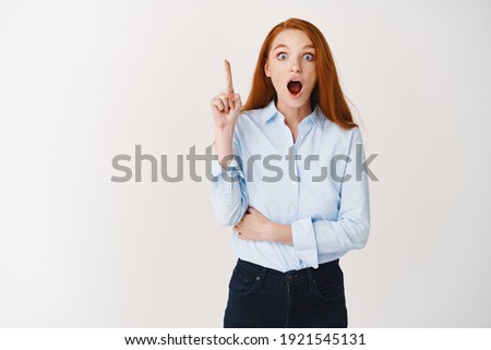 Business people. Excited redhead woman giving an idea, raising finger and saying suggestion, standing in blue collar shirt for office, white background.