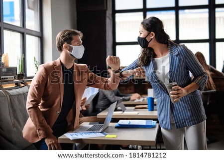 Business people with face masks greeting indoors in office, coronavirus concept.