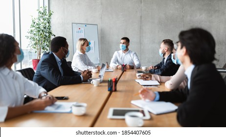 Business People In Face Masks Sitting At Desk During Corporate Meeting In Modern Office. Coworkers Safety, Virus Protection At Workplace Concept. Entrepreneurship And Covid-19 Coronavirus Pandemic