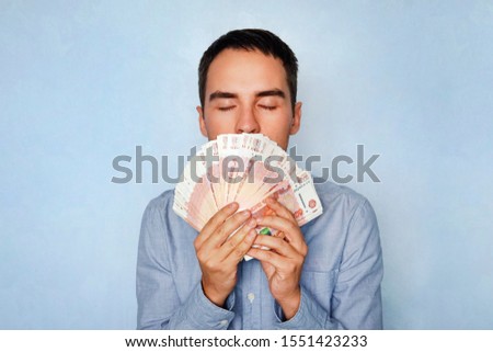 business, people and finances concept - businessman smelling Russian money. The sweet smell of money. Young guy sniffing 5000 rubles Earned money. Salary. Easy money.
