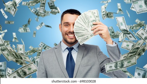 business, people and finances concept - smiling businessman with bundle of american dollar cash money over blue background - Shutterstock ID 698103028