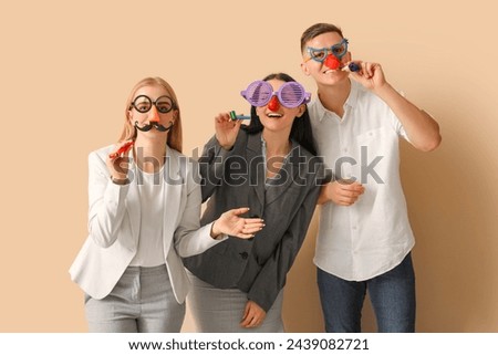 Business people in funny disguise with party whistles on beige background. April Fools' Day celebration