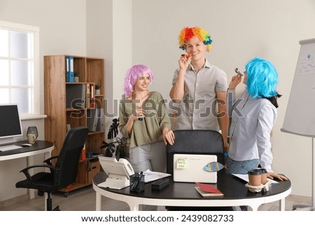 Business people with funny wigs and party whistles in office. April Fools' Day celebration