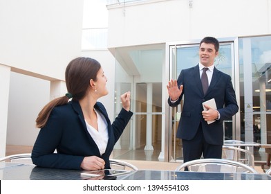 Business people gesturing and saying goodbye to each other outdoors. Business woman sitting at desk and man standing and waving his hand. Business people leave-taking concept.