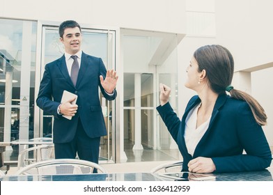 Business People Gesturing And Saying Goodbye To Each Other Outdoors. Business Woman Sitting At Desk And Man Standing And Waving His Hand. Business People Leave-taking Concept.