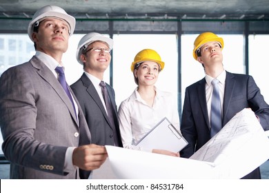 Business People In Hard Hats Looking Up At The Site