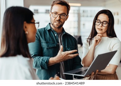 Business people having a discussion and using a laptop in an office. Team of business professionals standing together and having a meeting.