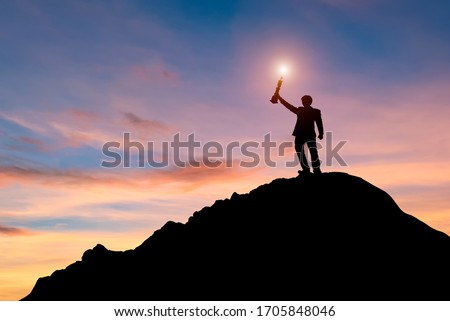 Business people holding trophies Victory success Success on top - Hipster business man on a hilltop holding a trophy in raised hands. Winner, happiness and reaching