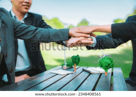 Business people join hand together as teamwork and unity, outdoor business meeting table. Eco-friendly practices and collaboration in corporate social responsibility for greener environment. Gyre