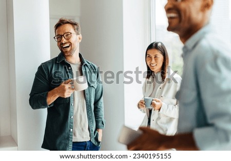 Business people laughing together during a coffee break at work. Group of young professionals standing together in an office.