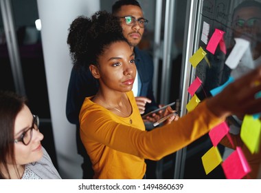 Business people in meeting brainstorming and discussing post it notes stuck on glass wall at office - Shutterstock ID 1494860639