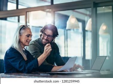 Business people meeting in office and discussing over a documents. Business woman with a financial report in hand sitting with male colleague looking at her and smiling. - Powered by Shutterstock