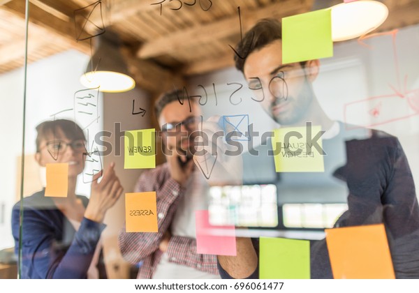 Business people meeting at office and use post it\
notes to share idea. Brainstorming concept. Sticky note on glass\
wall.