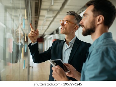 Business people meeting planning start up, talking, discussing ideas, brainstorming. Scrum master using sticky notes standing near planning board in modern office. Agile methodology, scrum concept	 - Shutterstock ID 1957976245