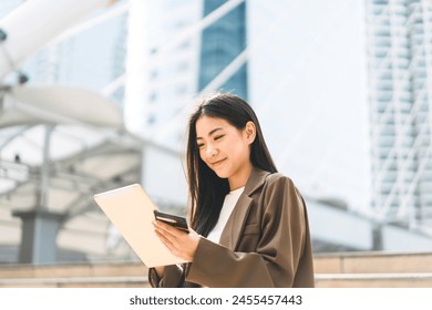 Business people modern urban lifestyles with technology. Asian woman using digital tablet for internet browsing or app. Wearing brown suit casual cloth. City background. - Powered by Shutterstock