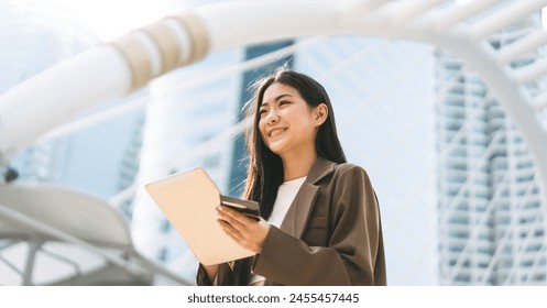 Business people modern urban lifestyles with technology. Asian woman using digital tablet for internet browsing or app. Wearing brown suit casual cloth. City background. - Powered by Shutterstock