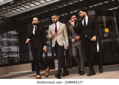 Business People Outdoor Meeting, A Group Of Male Businessmen In Suits Exit The Front Door Of A Glass Building. Working Break. Teamwork And Brainstorming. Successful Teamwork