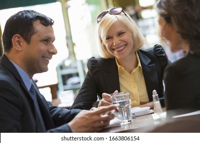 Business People Outdoors, Keeping In Touch While On The Go. Three People, A Man And Two Women Sitting At A Table. A Meeting Or Social Gathering.