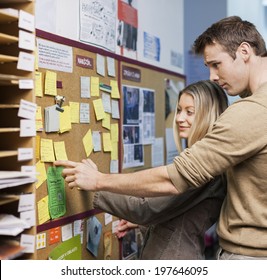 Business People Reading Reminders On Bulletin Board In Office