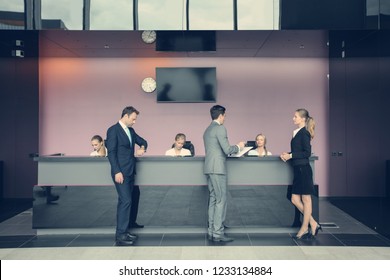 Business People At Reception Or Front Desk In Office Building, Hotel Or Airport