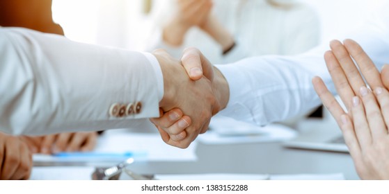 Business people shaking hands at meeting while theirs colleagues clapping and applauding. Group of unknown businessmen and women in modern white office. Success teamwork, partnership and handshake - Shutterstock ID 1383152288